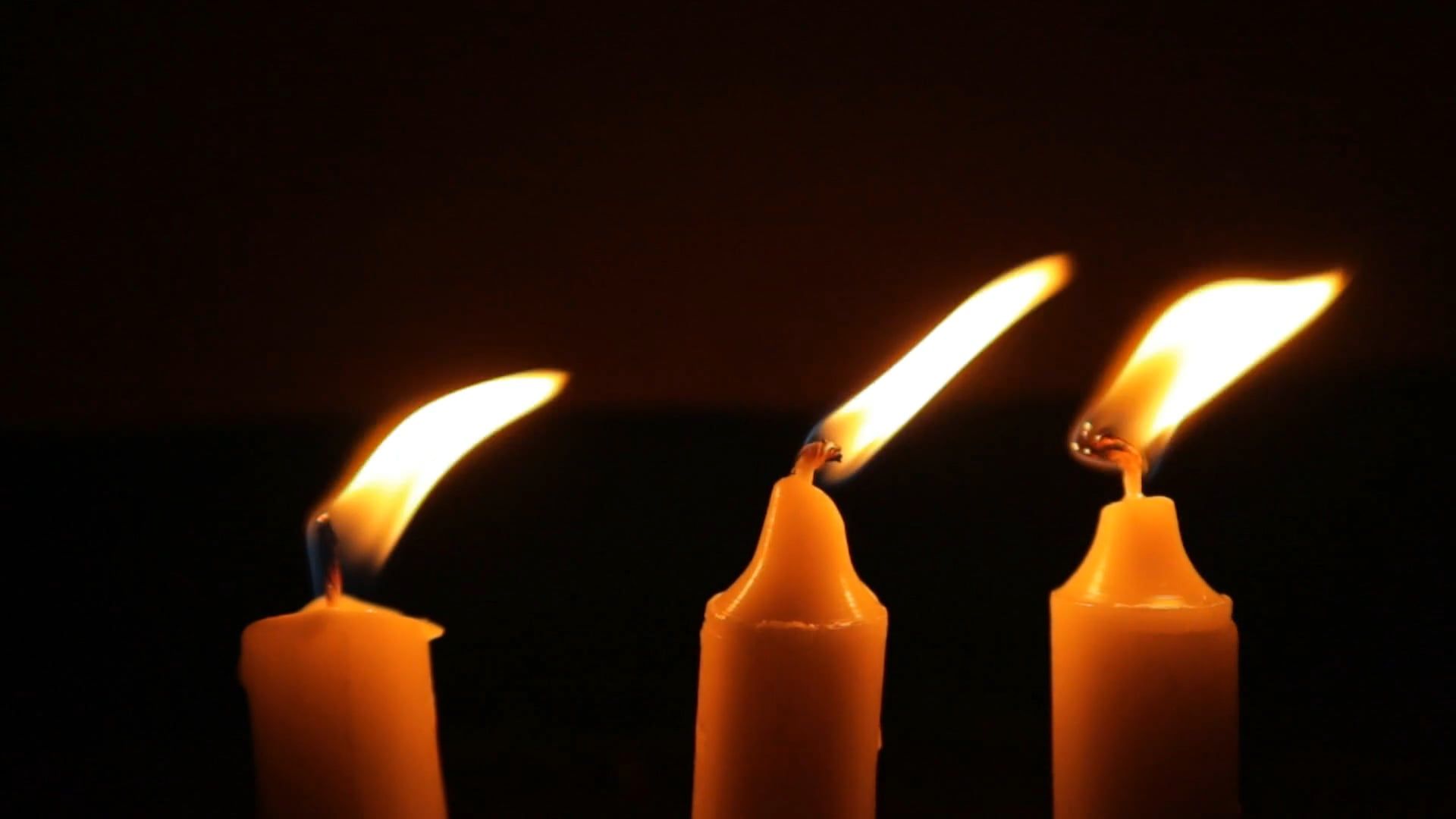 Close-up of candle flames flickering gently in a darkened setting, 13s (no faces)