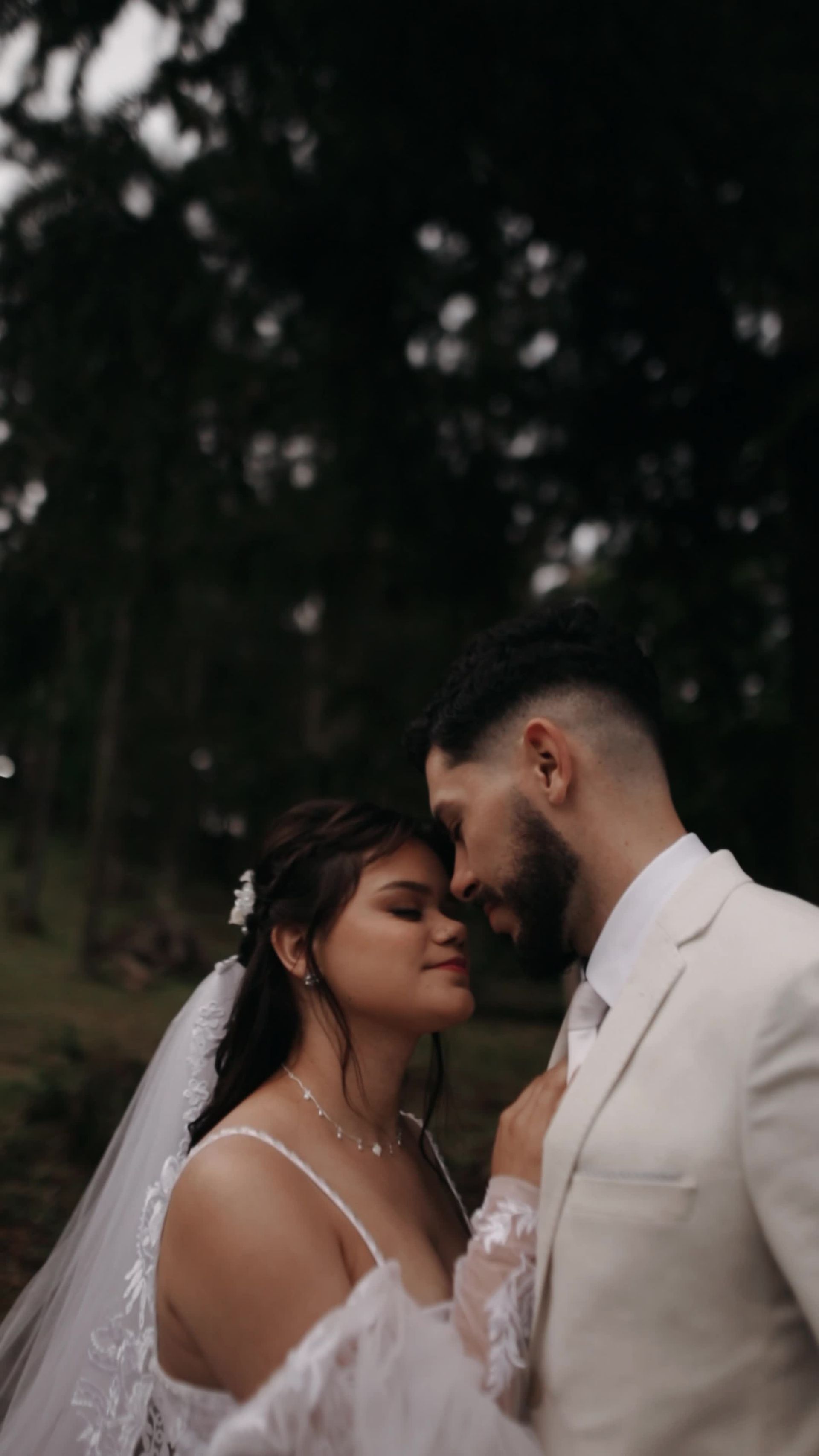 A bride and groom share a tender moment in a lush outdoor setting, 18s, 9:16